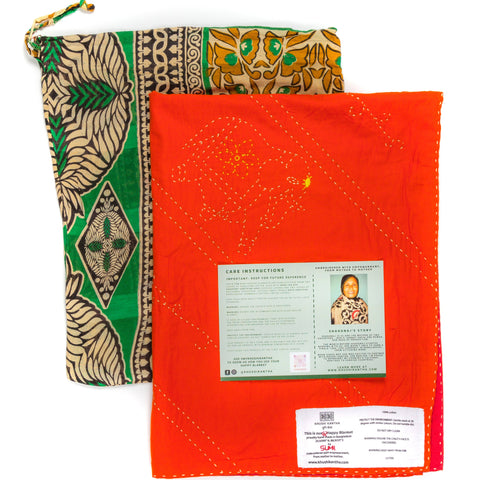 Orange fabric blanket with labels and a green and gold patterned bag on a white background