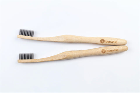 Two bamboo toothbrushes for adults from beewise soft charcoal bristles on top of the sink of a bathroom