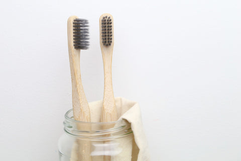 Two bamboo toothbrushes for adults from beewise soft charcoal bristles inside a glass container in the bathroom