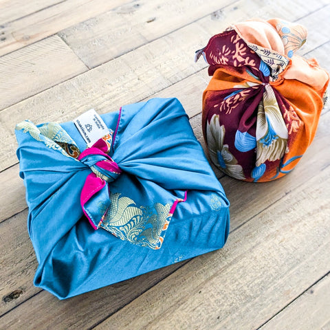 Two wrapped packages on a wooden surface, one blue with gold patterns and the other multicolored.