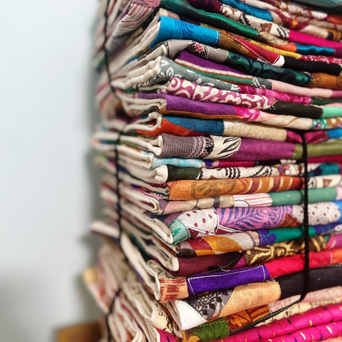 Stack of sari patchwork cushion covers piled on a wooden surface against a white wall