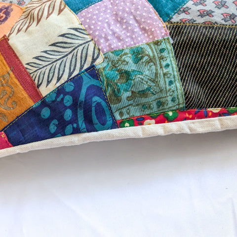 Close up view of sari patchwork cushion cover on a pillow, laying on white surface