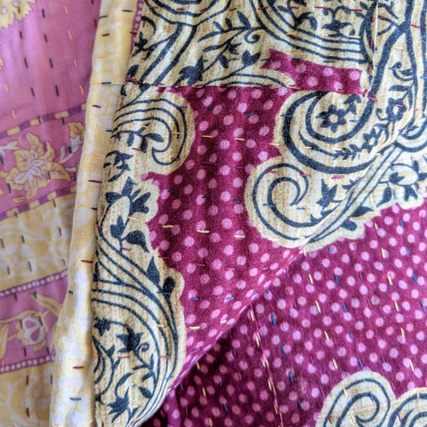 Close-up of a pink and yellow patterned fabric kantha quilt with intricate designs.