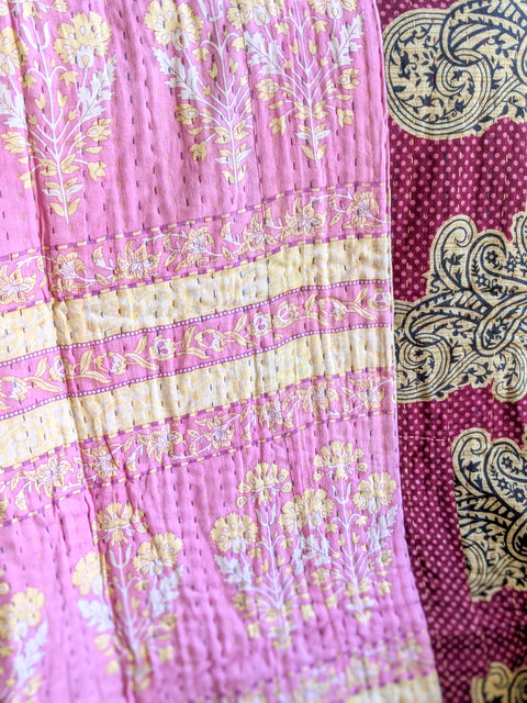 Close-up of a pink and yellow patterned fabric kantha quilt with intricate designs.