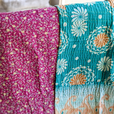 Two sides of one blanket with floral-patterned fabrics, one pink and one teal with orange and white designs, draped over a surface.