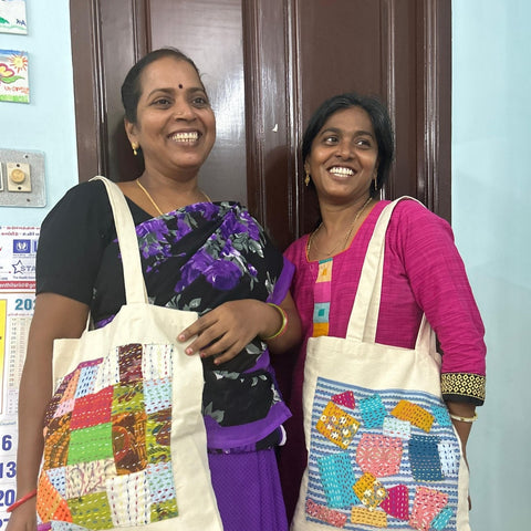 smiling artisans modelling square design sari patchwork cotton tote bags against brown door and blue wall