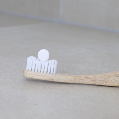 zero waste & sustainable toothpaste tablet on top of a white bristles bamboo toothbrush