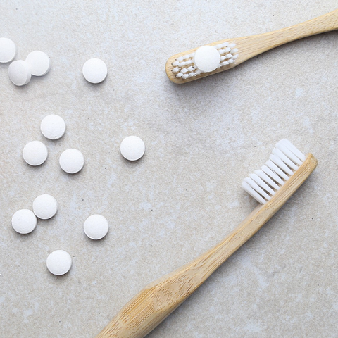 toothpaste tablets spread on the floor and also on top of a white bristles bamboo toothbrush with peppermint flavour